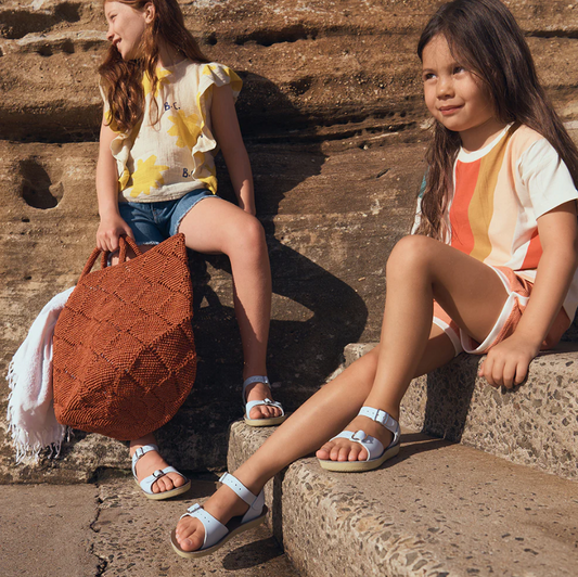Two young girls sitting on stone steps with a woven bag.
