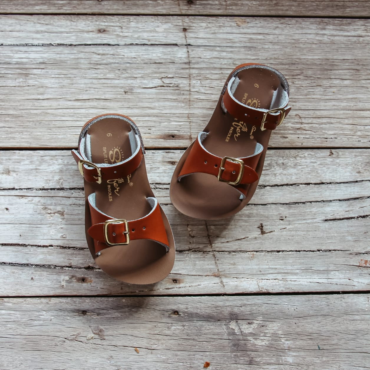 Pair of brown sandals with buckles on a wooden surface