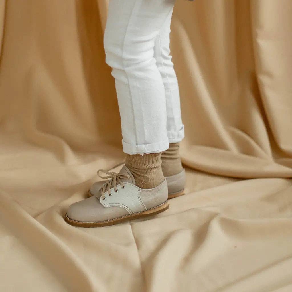 Person wearing white sneakers and white pants on a beige fabric background zimmerman kids shoes