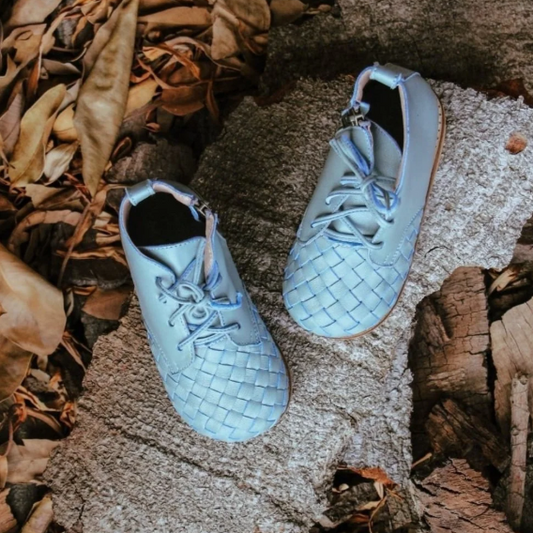 Pair of light blue woven shoes on a textured surface with leaves and wood.