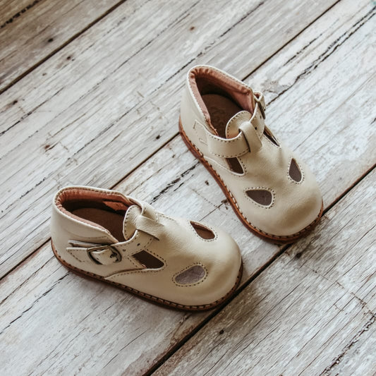 Pair of beige children's sandals on a wooden floor