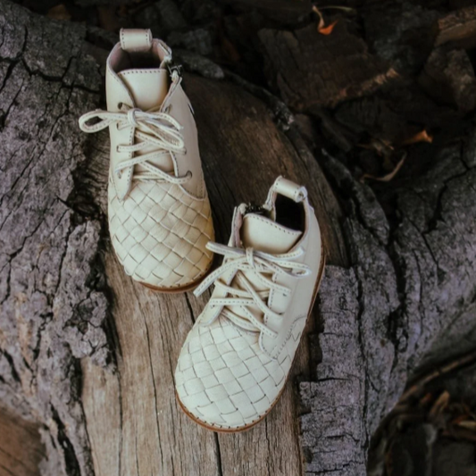 Pair of beige leather shoes with woven pattern on a wooden surface