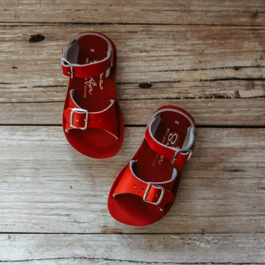 Red sandals with silver buckles on a wooden surface