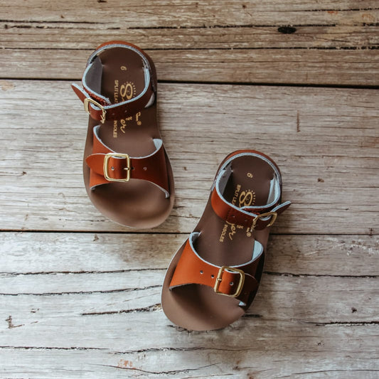 Pair of brown leather sandals with buckles on a wooden surface